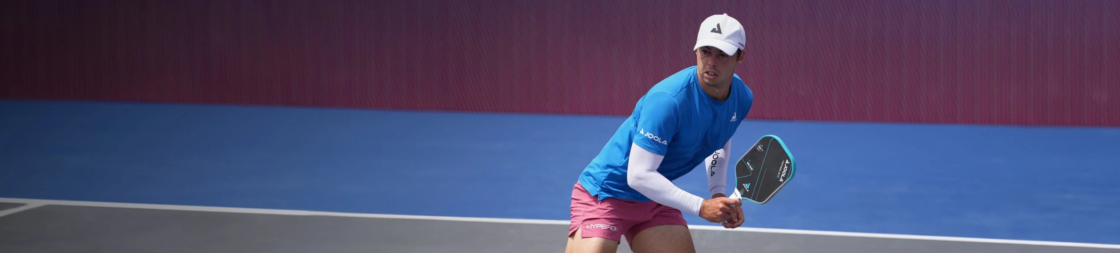 Pickleball player in action on court with paddle, wearing athletic gear and cap
