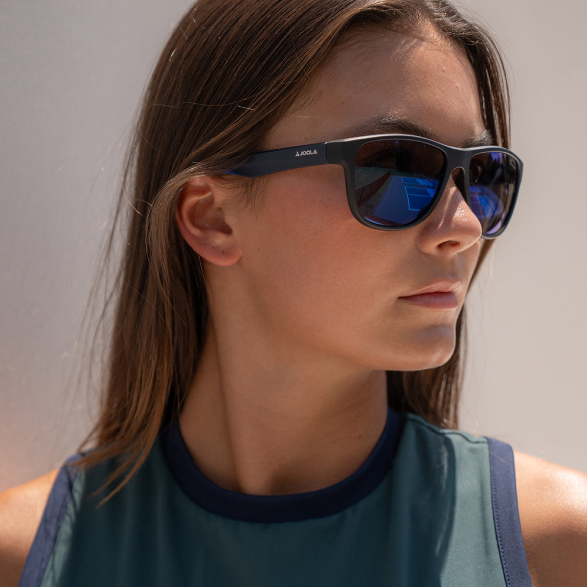 Woman wearing JOOLA sport sunglasses with blue mirrored lenses, ideal for pickleball and table tennis.