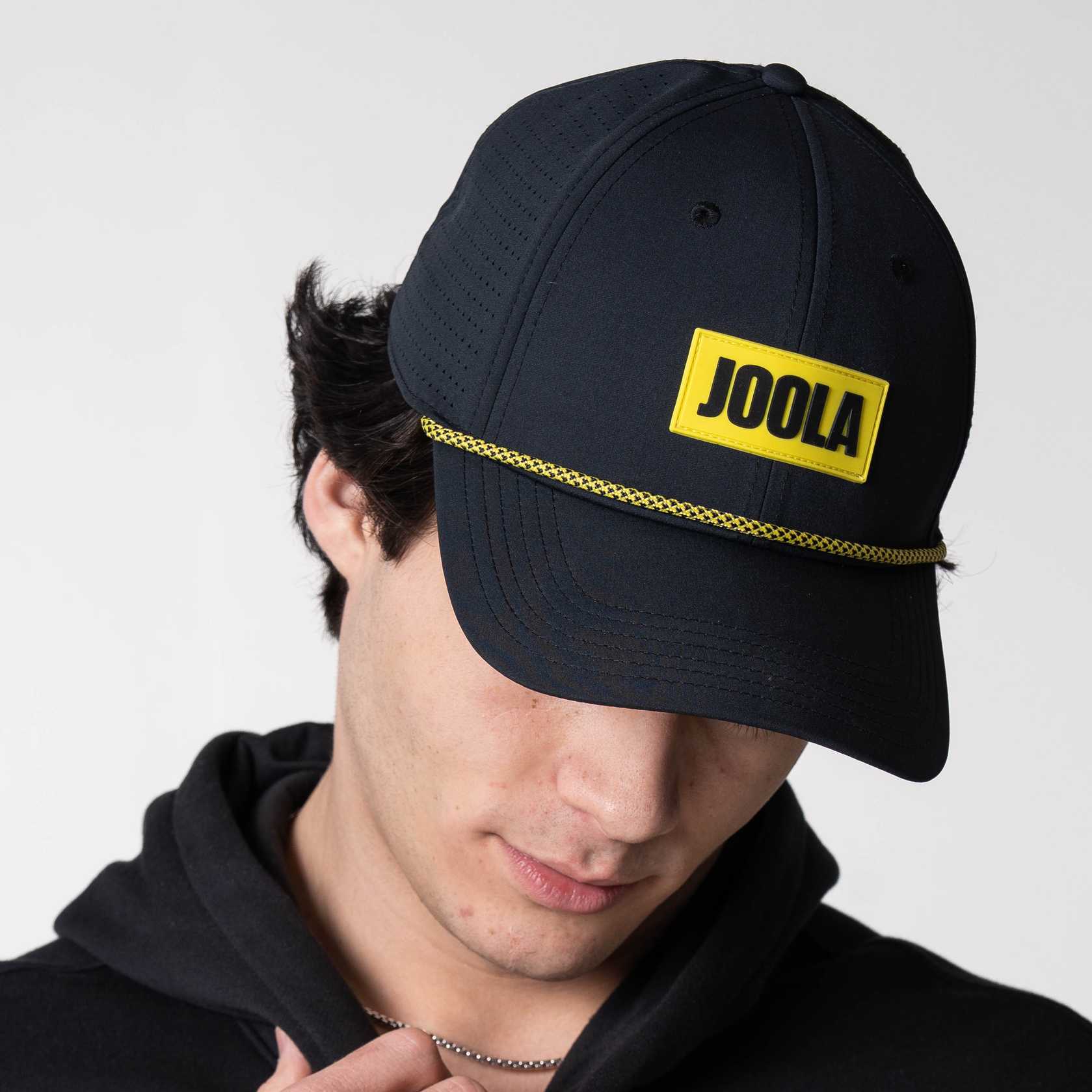 Person wearing a JOOLA Rope Cap, black with yellow branding.