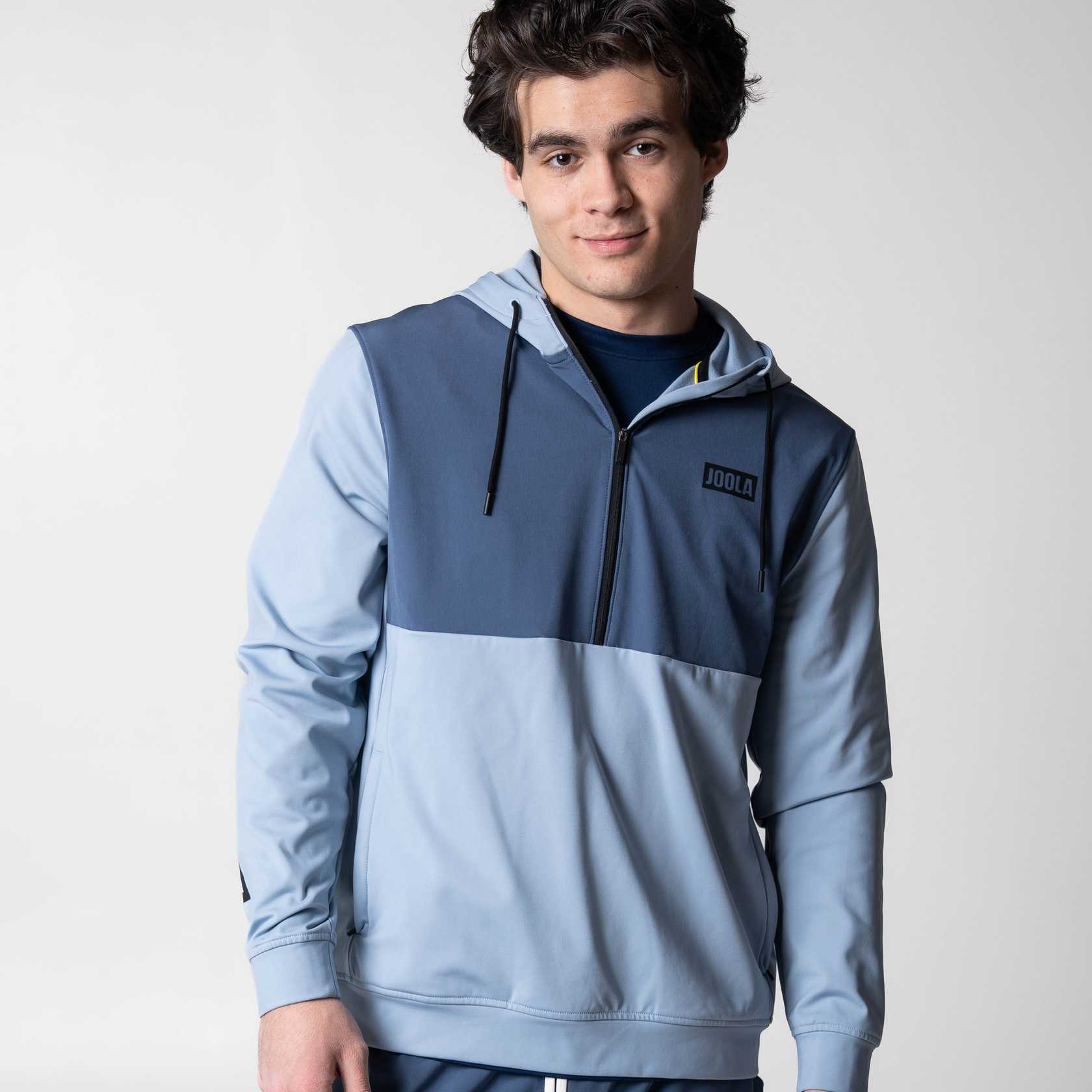 Person wearing a two-tone blue and hoodie on a plain background.